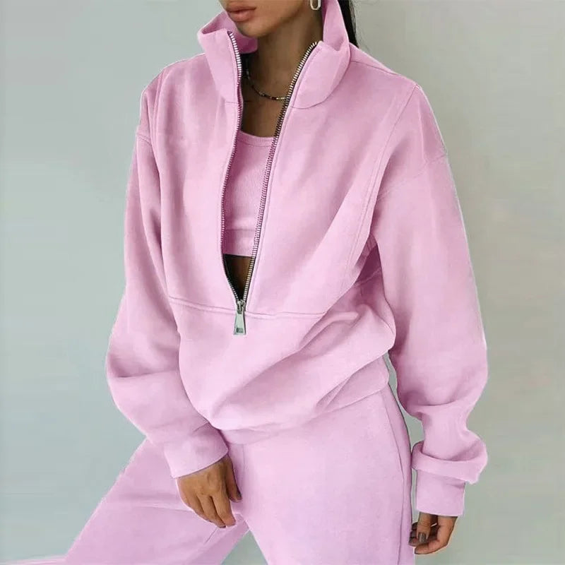 Une femme porte un ensemble décontracté rose, composé d'un haut à zip et d'un pantalon assorti. Le haut a un col zippé qui lui donne un look moderne et confortable, parfait pour un style décontracté et hivernal.